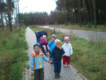 Dzieci spacerują chodnikiem, widać las