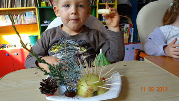 Dziecko dumne ze swojego dzieła, jeż z połowy jabłka i wykałaczek